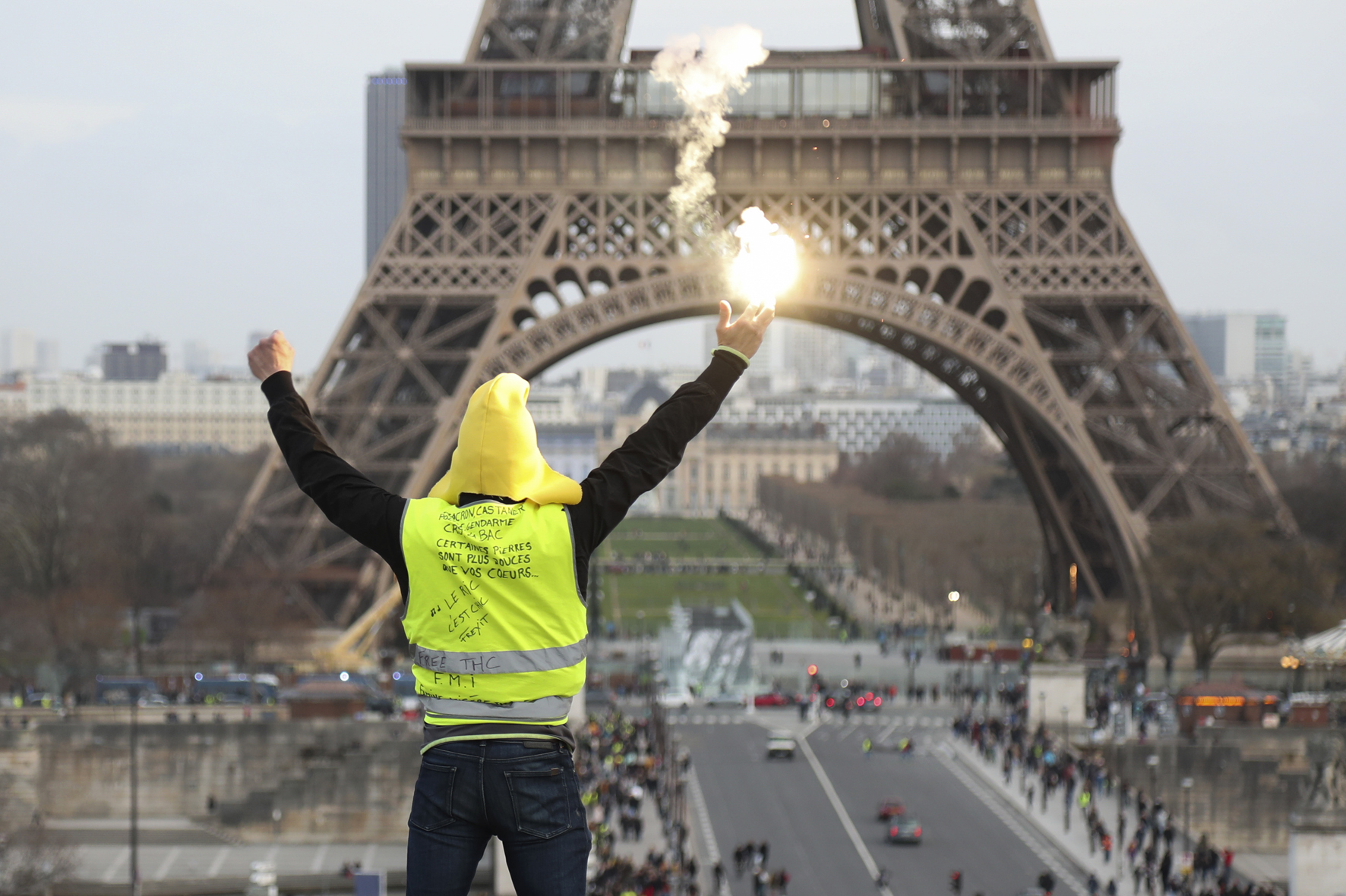 A protester holding a flare gestures in front of the Eiffel Tower during a demonstration in Paris on February 9, 2019, as the "Yellow Vests" (Gilets Jaunes) protesters take to the streets for the 13th consecutive Saturday. - The "Yellow Vests" (Gilets Jaunes) movement in France originally started as a protest about planned fuel hikes but has morphed into a mass protest against the French President's policies and top-down style of governing. (Photo by Zakaria ABDELKAFI / AFP)