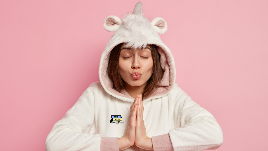 Ragazza su sfondo rosa in posa meditativa che indossa un pigiama con cappuccio da unicorno peloso